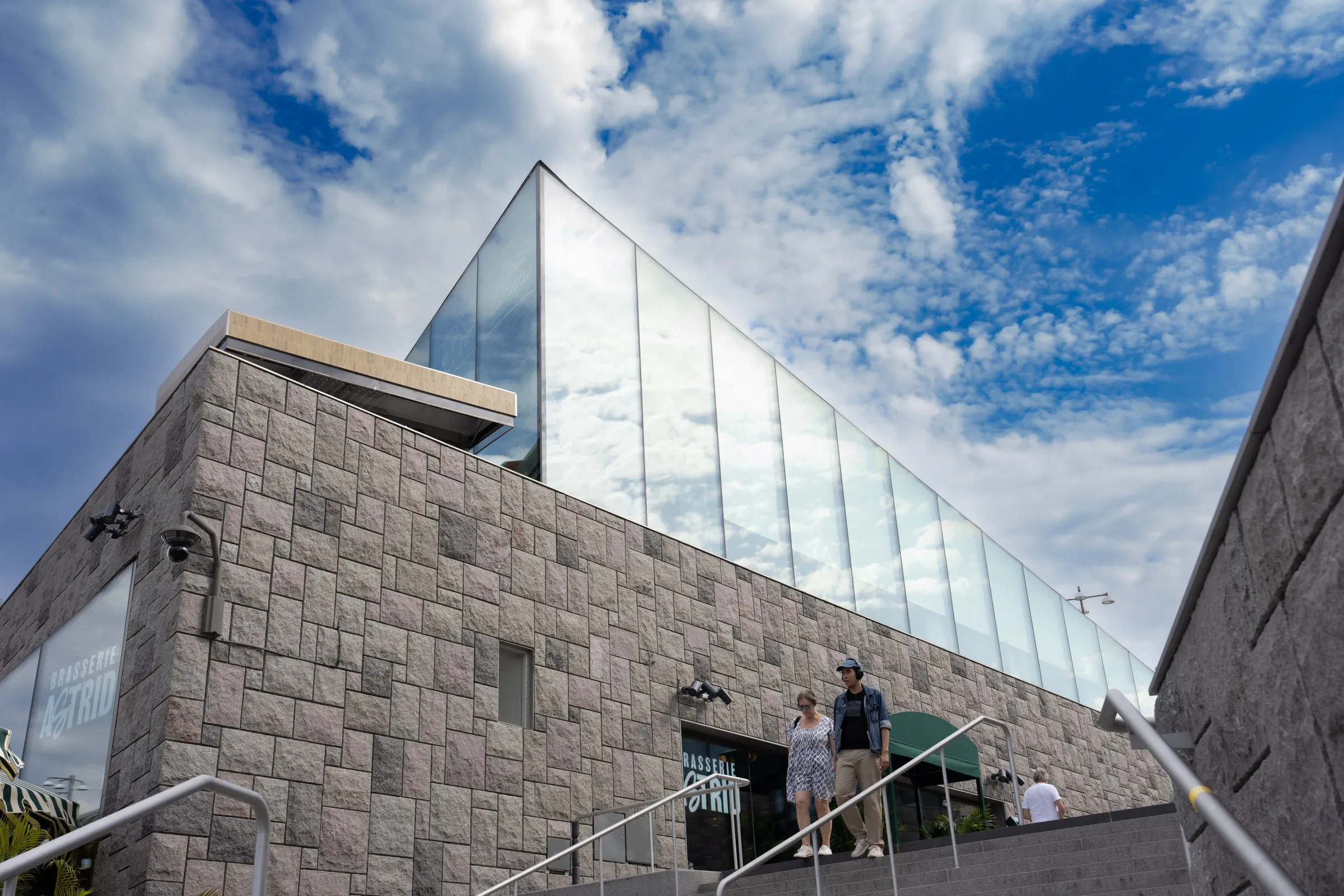 A modern stone building rises toward a cloud-filled sky