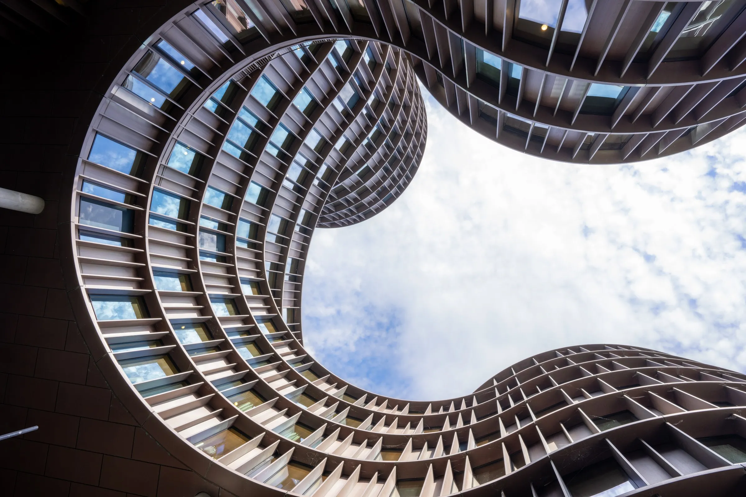 A curving modern facade framing a patch of cloud-filled sky